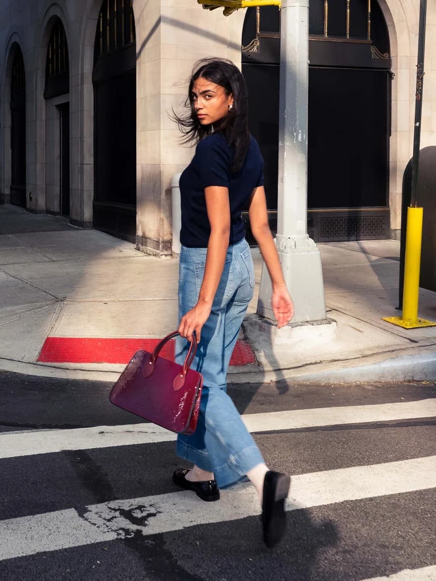 Woman crossing a city street carrying a red Cambridge Satchel handbag