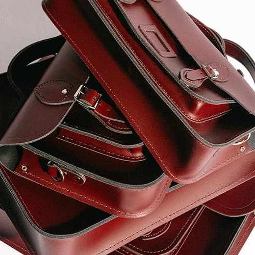 Stacked burgundy leather satchels showing classic Cambridge Satchel design