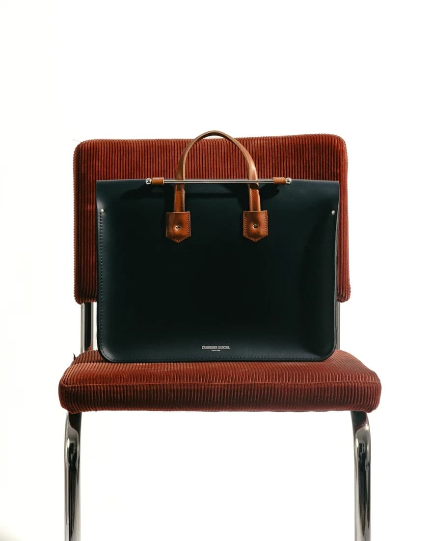 Black leather tote bag displayed on a corduroy chair, showing clean lines and quality leather