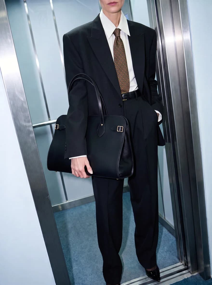 Model carrying a Cambridge Satchel leather bag in a sleek elevator interior